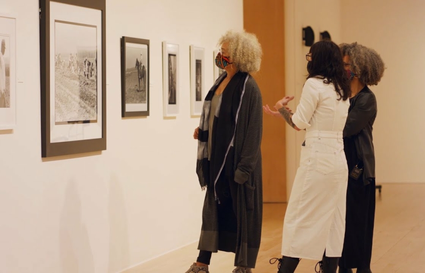 Angela Davis stands with 2 people looking at black and white photographs