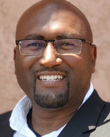 Close up image of bald man with closely cropped facial hair and glasses wearing a suit jacket smiling
