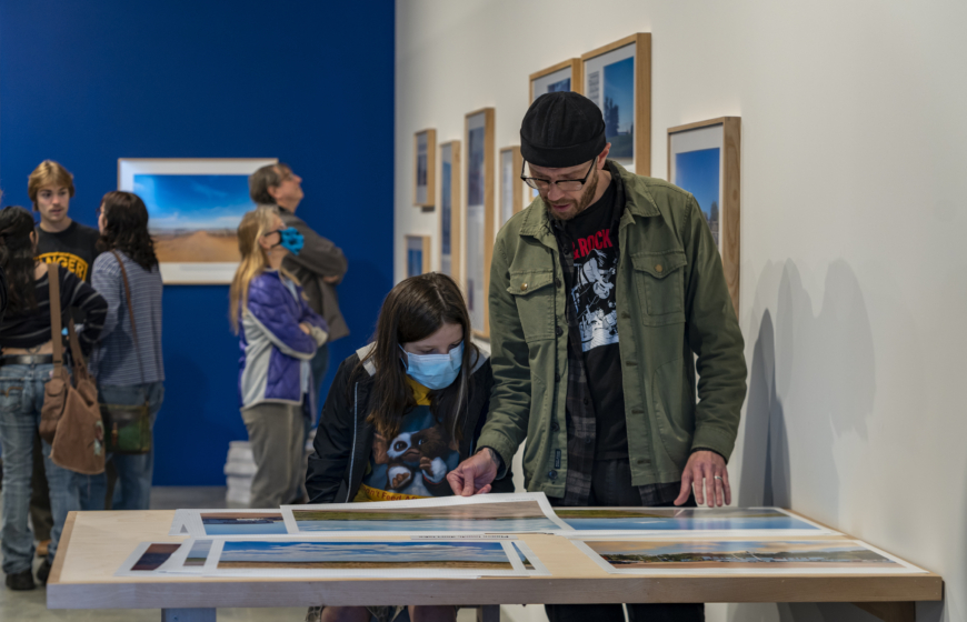 Two people stand at a table looking through poster sized images of landscapes