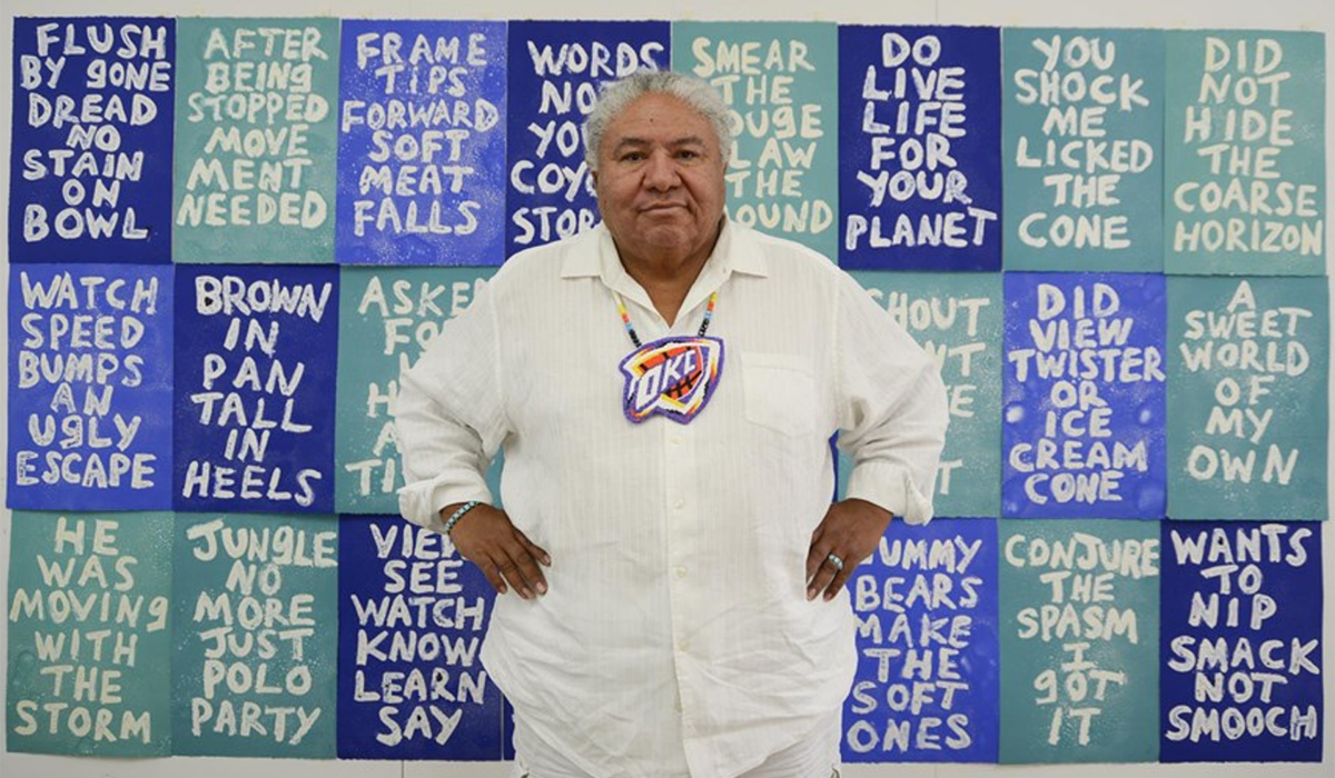 A Native American man stands in front of an art installation.