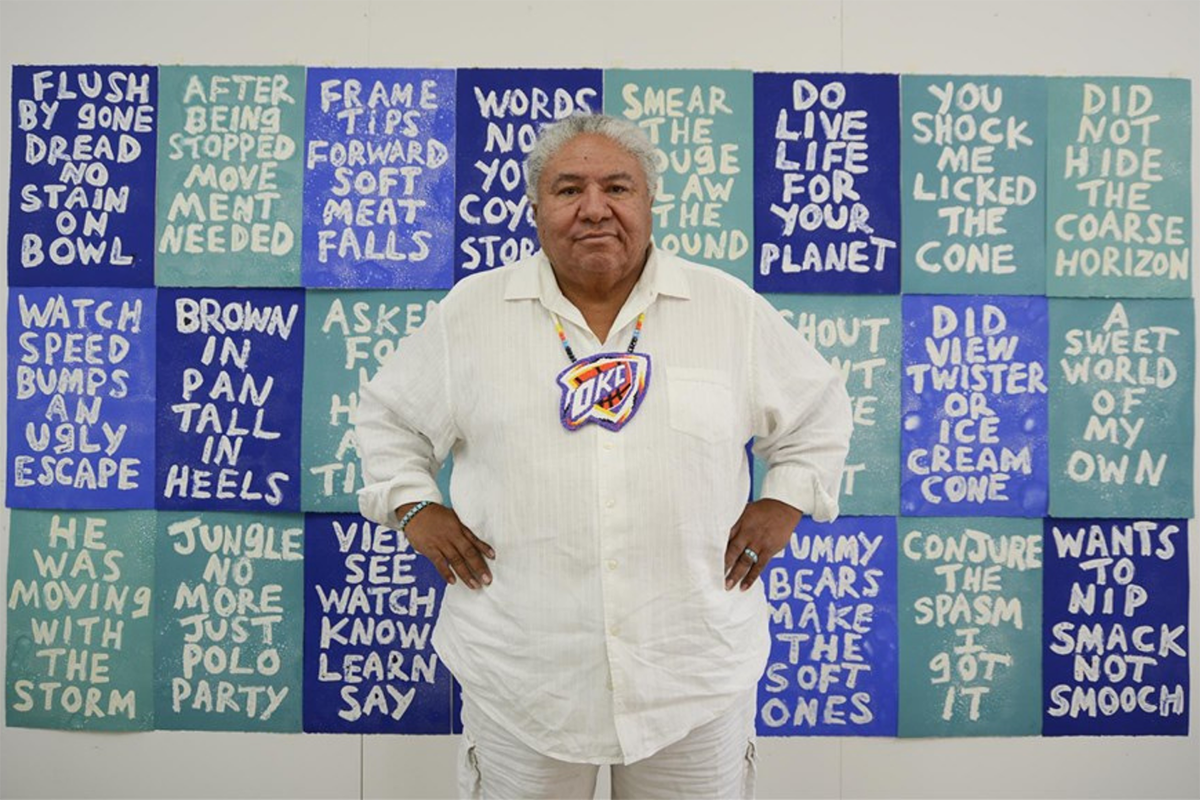 A Native American man stands in front of an art installation.