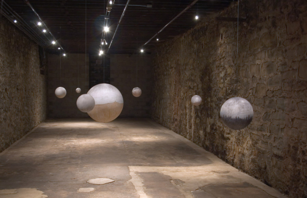Silver globes are suspended from the ceiling in an art exhibit.