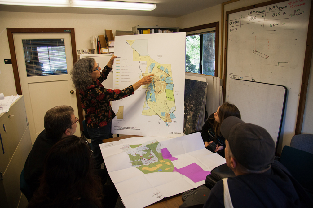 A woman points at a map while students look on.