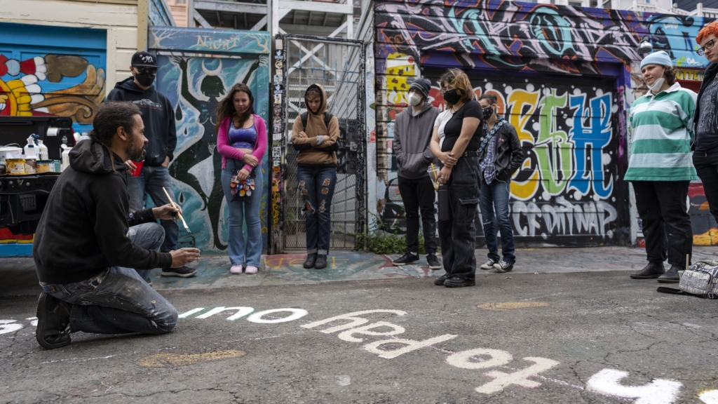 Students speaking with artist in Clarion Alley, surrounding by wall mural