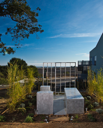 a sculpture of a prison cell sits surrounded by plants on a hill overlooking the ocean