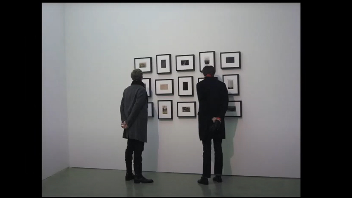 Two people look at artwork displayed on a white wall.