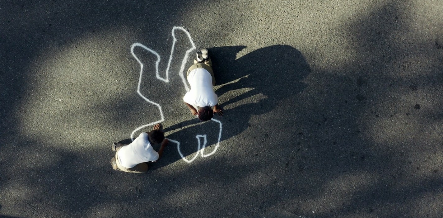 Two people draw a chalk outline of a body.