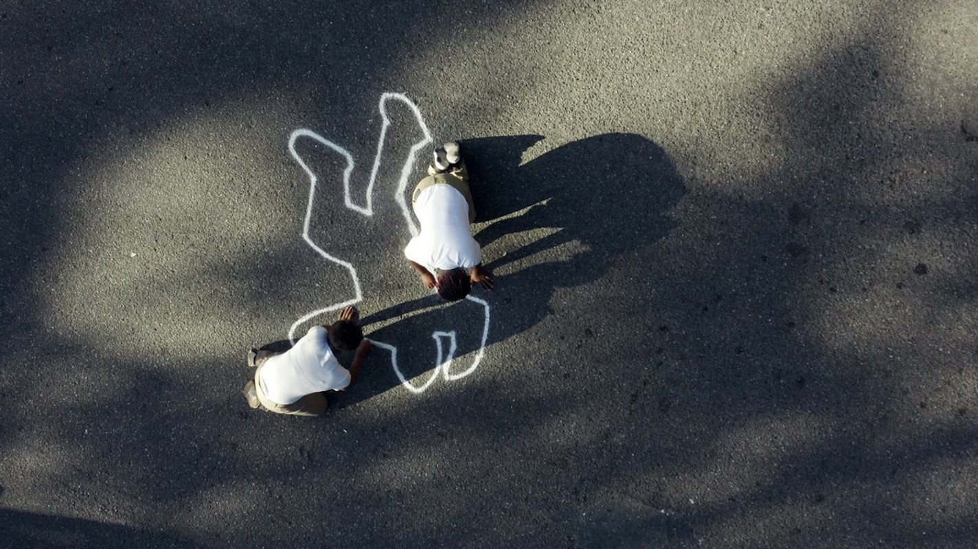 Two people draw a chalk outline of a body.