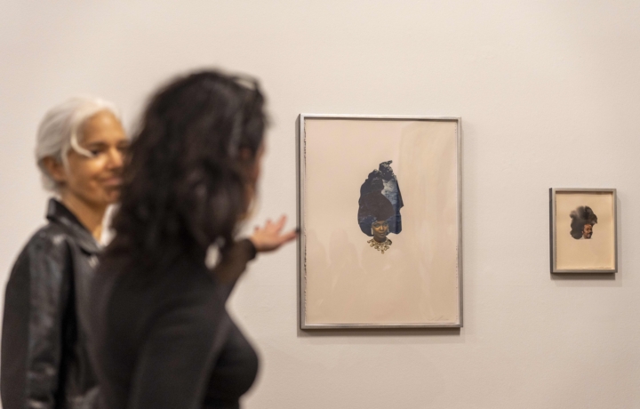 Two woman gesture at a small collage featuring a woman with an iceberg on her head