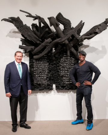 two people wearing black standing in front of a wall relief sculpture