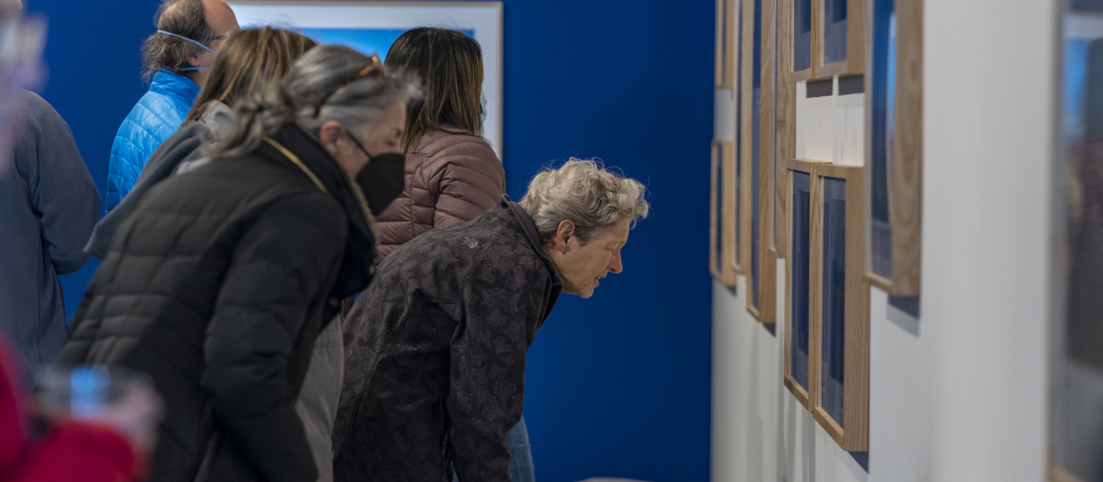 A woman looks closely at a wall full of photographs by Ashley Hunt.