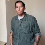MAn with denim shirt with rolled up sleeves and tattoos on his forearms.