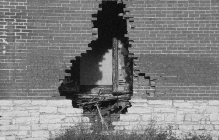 Black and white film still showing a large hole in a brick wall.