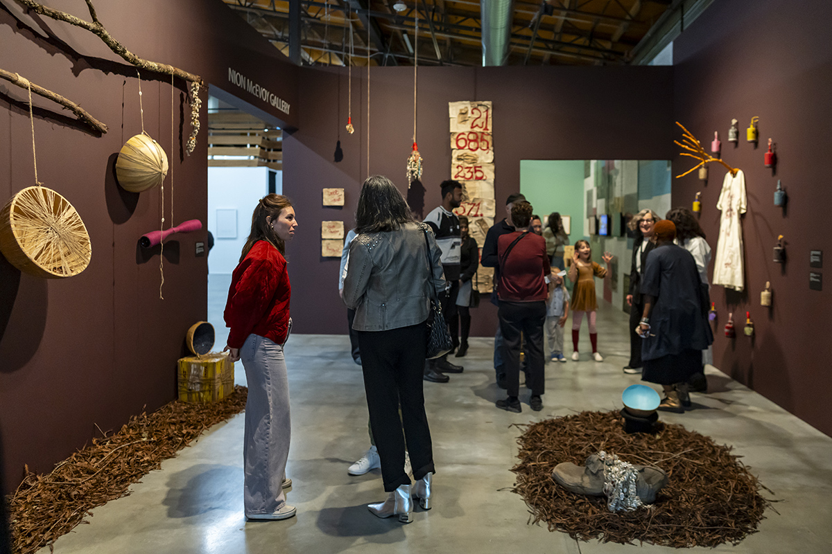 A group of people in a gallery space with dark maroon walls and a selection of art installations.